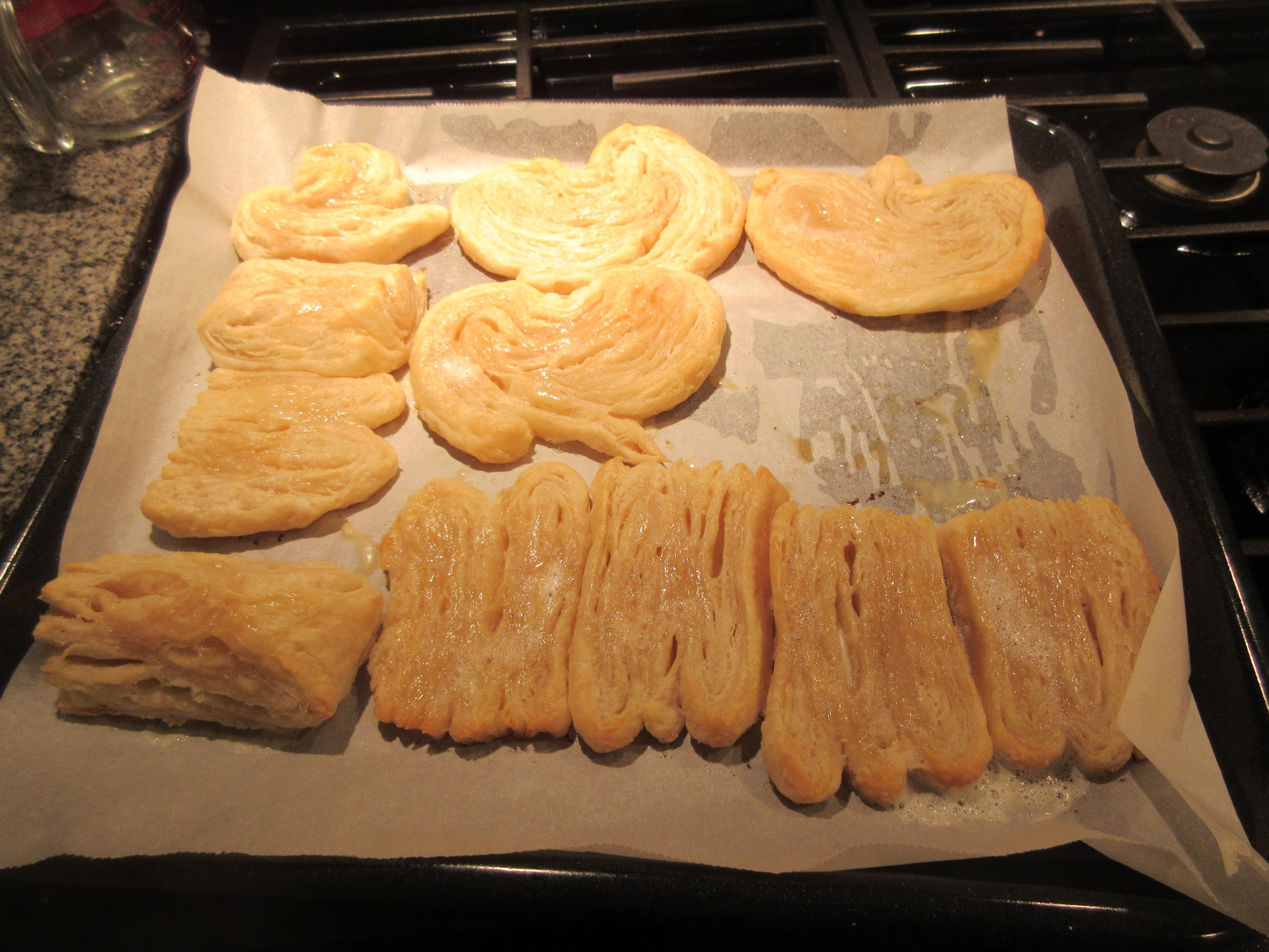 A baking tray of freshly baked puff pastry pieces on parchment, showing flaky laminated layers