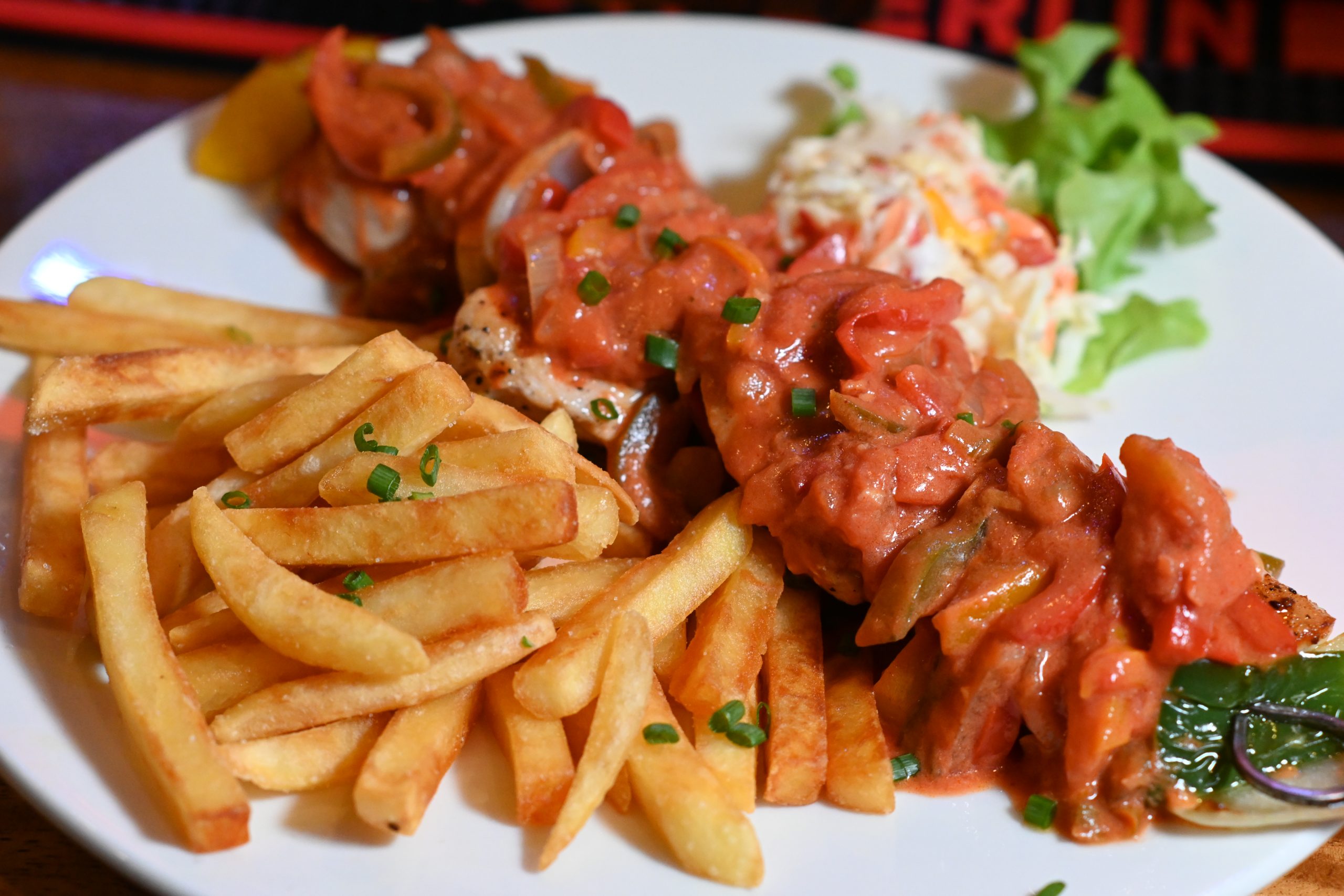 Plate of grilled skewered meat in tomato sauce with fries and a small side salad