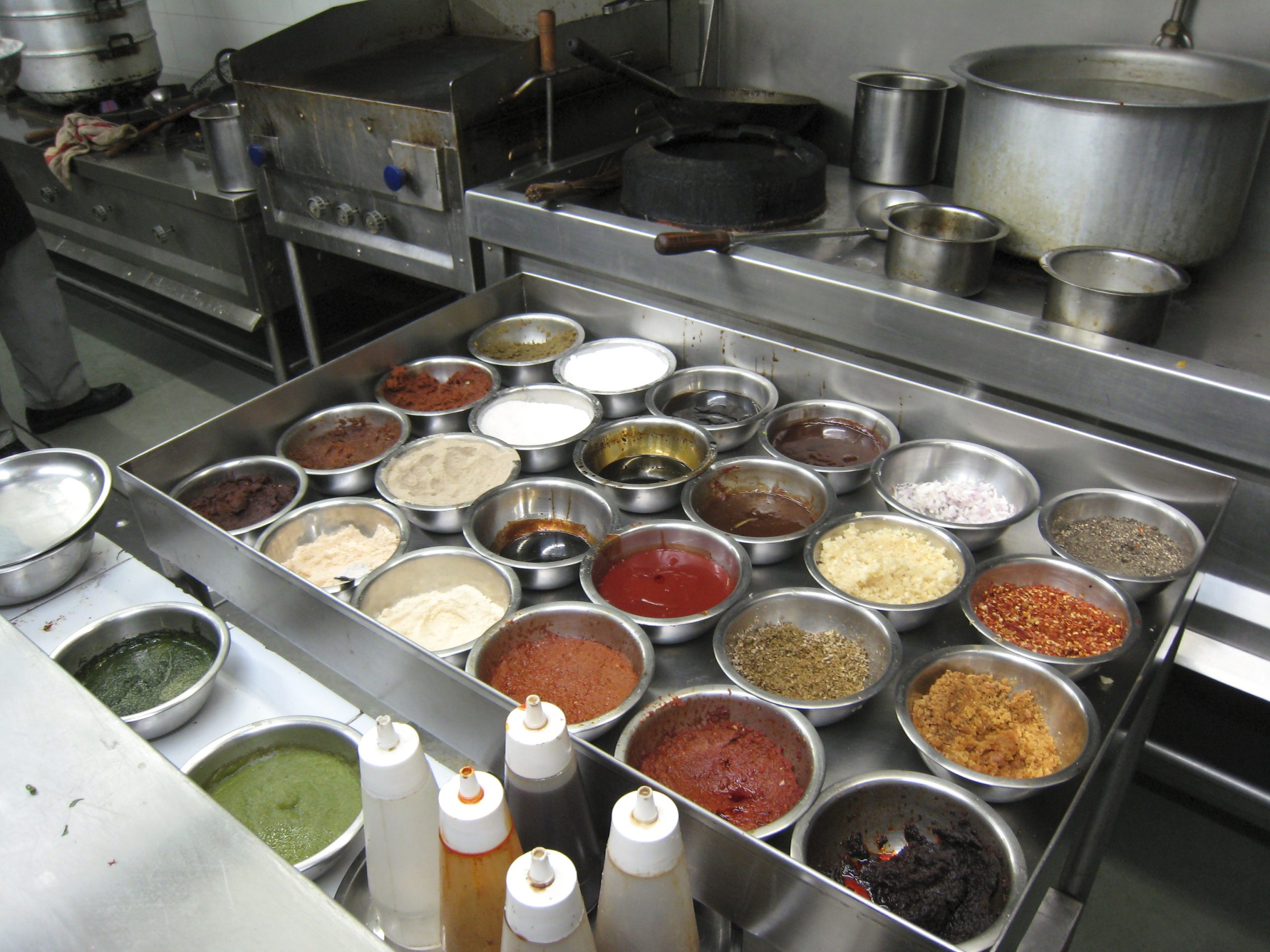 A hot station mise en place: rows of steel containers filled with sauces, garnishes and chopped ingredients beside a range
