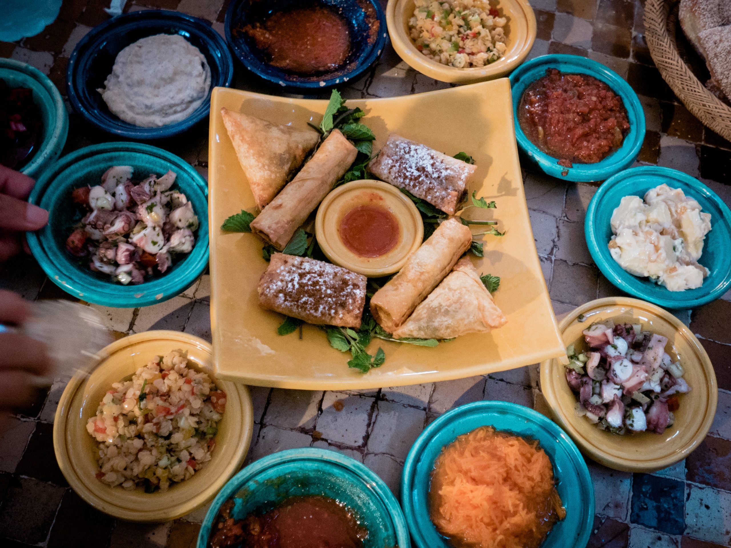 A spread of small appetizer plates with dips, pastries and vegetables on a patterned table