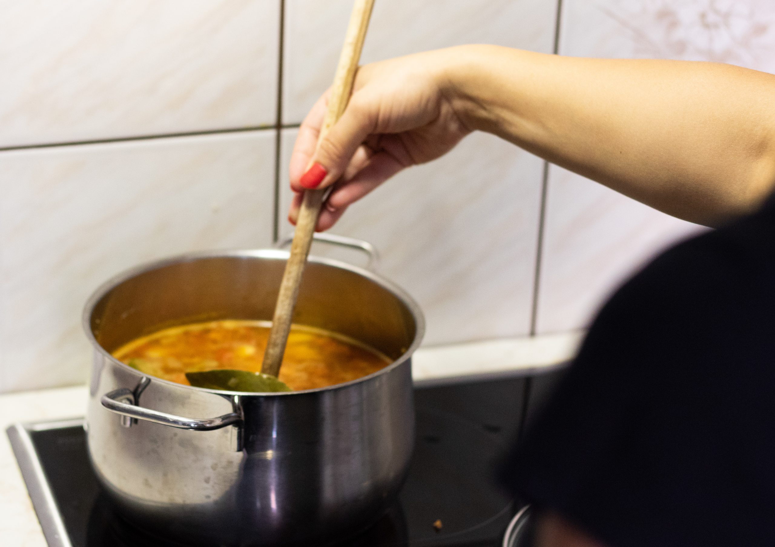 A cook stirring a large pot of soup with a long wooden spoon