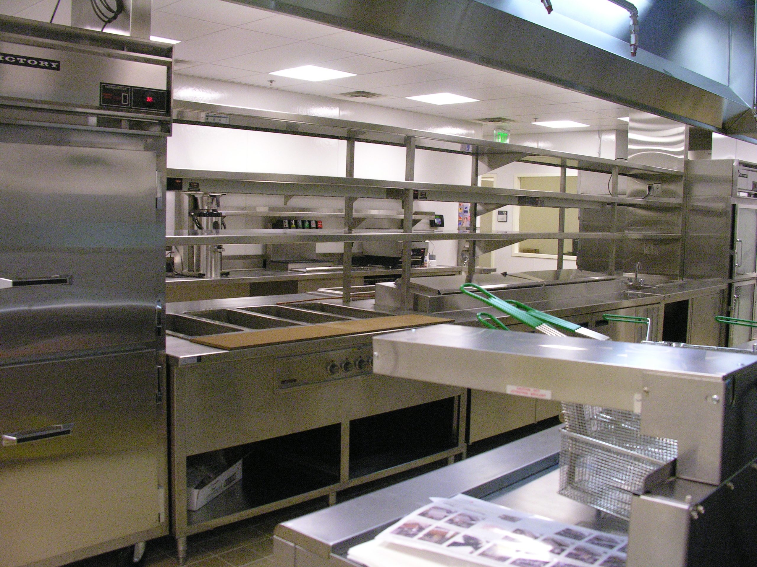 Empty commercial kitchen with stainless steel counters, shelving and refrigerators