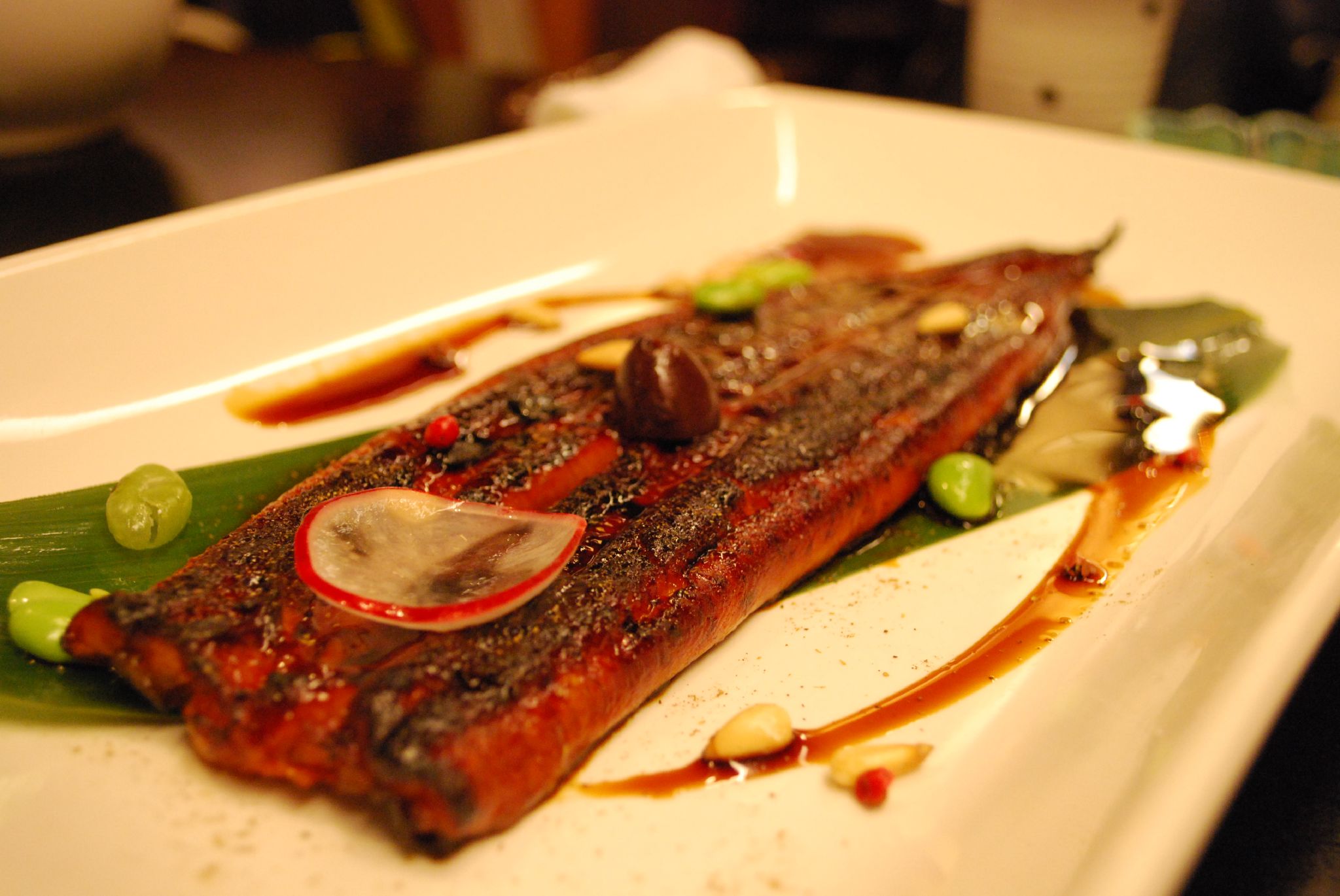 Plated fillet of glazed grilled eel with garnish on a white rectangular plate