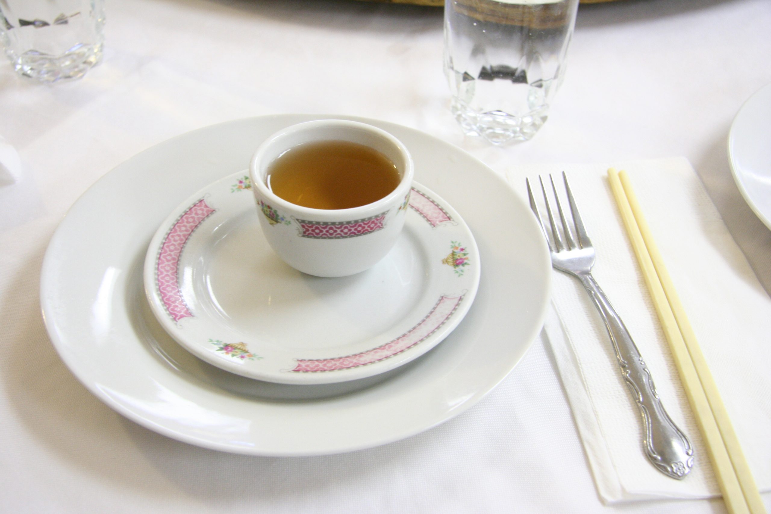 Restaurant place setting with a teacup on a saucer, a white plate, a fork and chopsticks on a napkin