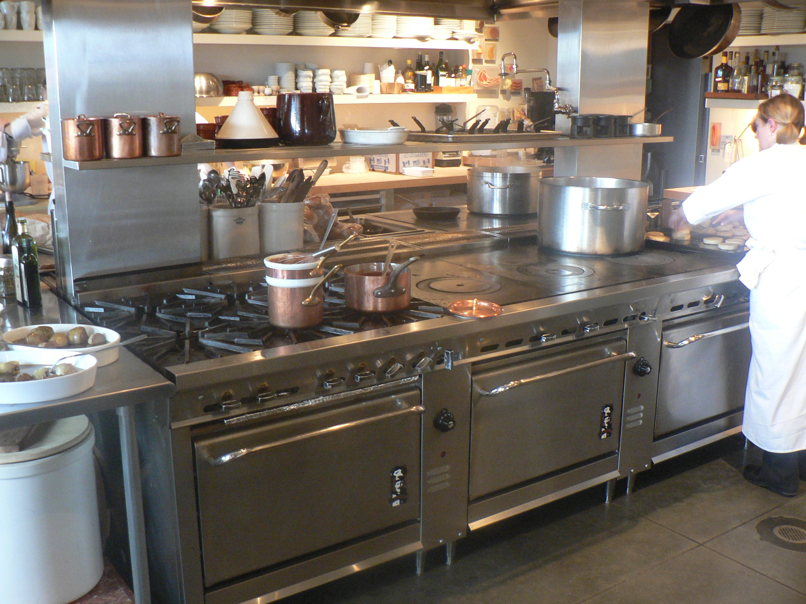 Cook working at a large professional range with copper pans and stockpots on the hot station of a restaurant kitchen