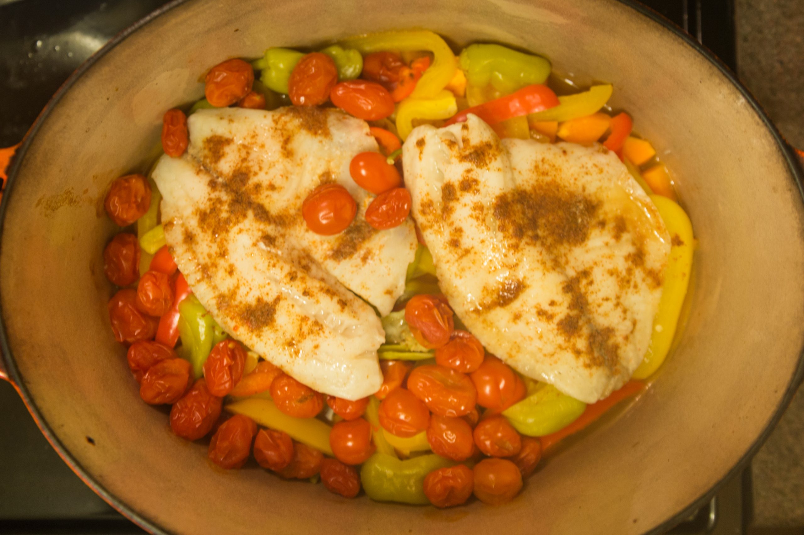 White fish fillets baked on a bed of cherry tomatoes and sweet peppers in an oval dish