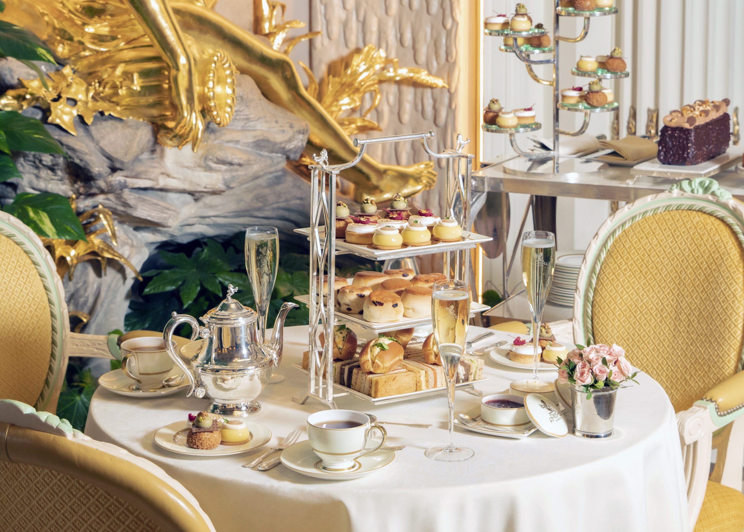 A hotel lounge table set for afternoon tea with tiered cake stands, teapot and glasses