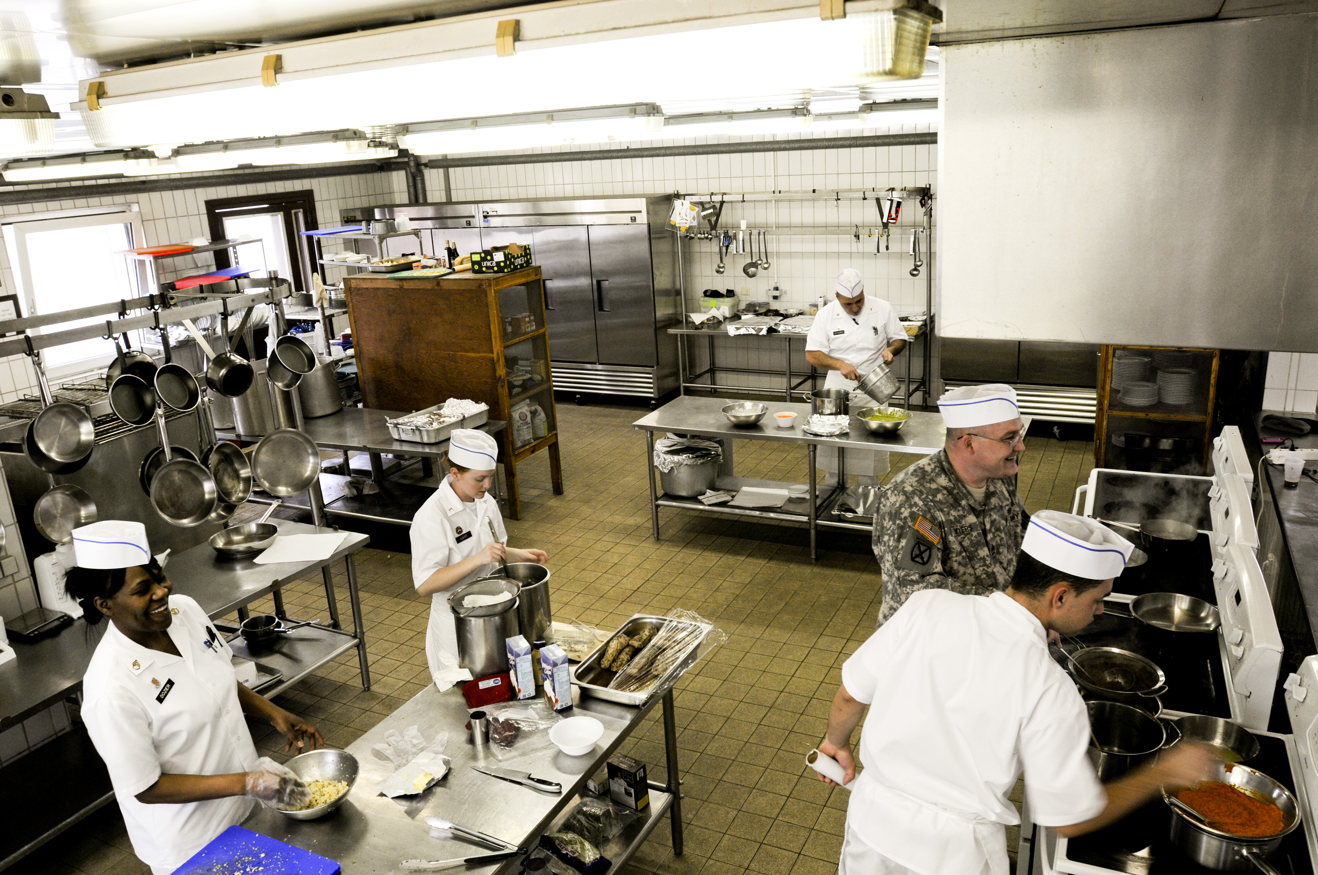 Cooks in white jackets and paper hats working at stations in a busy professional kitchen