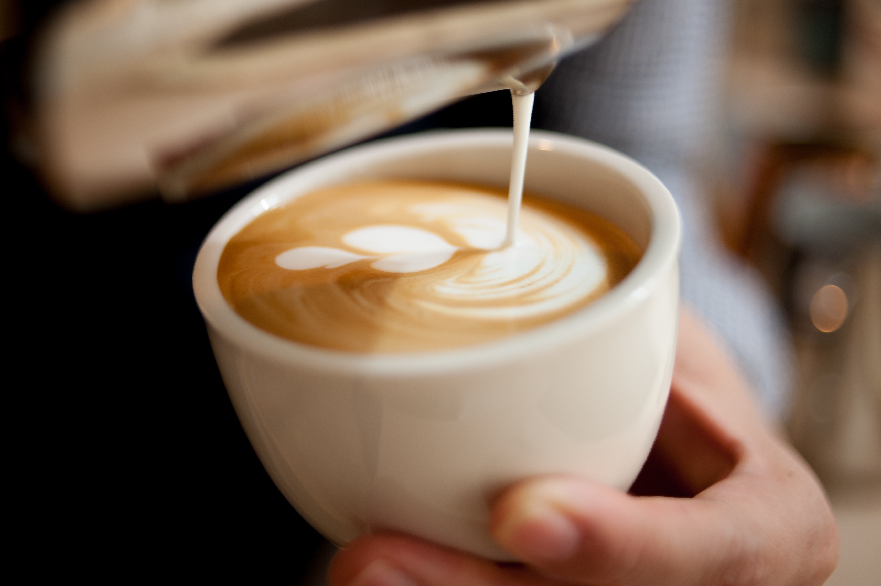 Steamed milk being poured into an espresso cup to form a latte art pattern