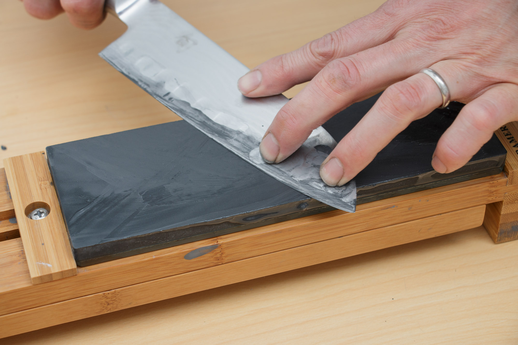 Hands sharpening a chef's knife on a whetstone set in a wooden holder
