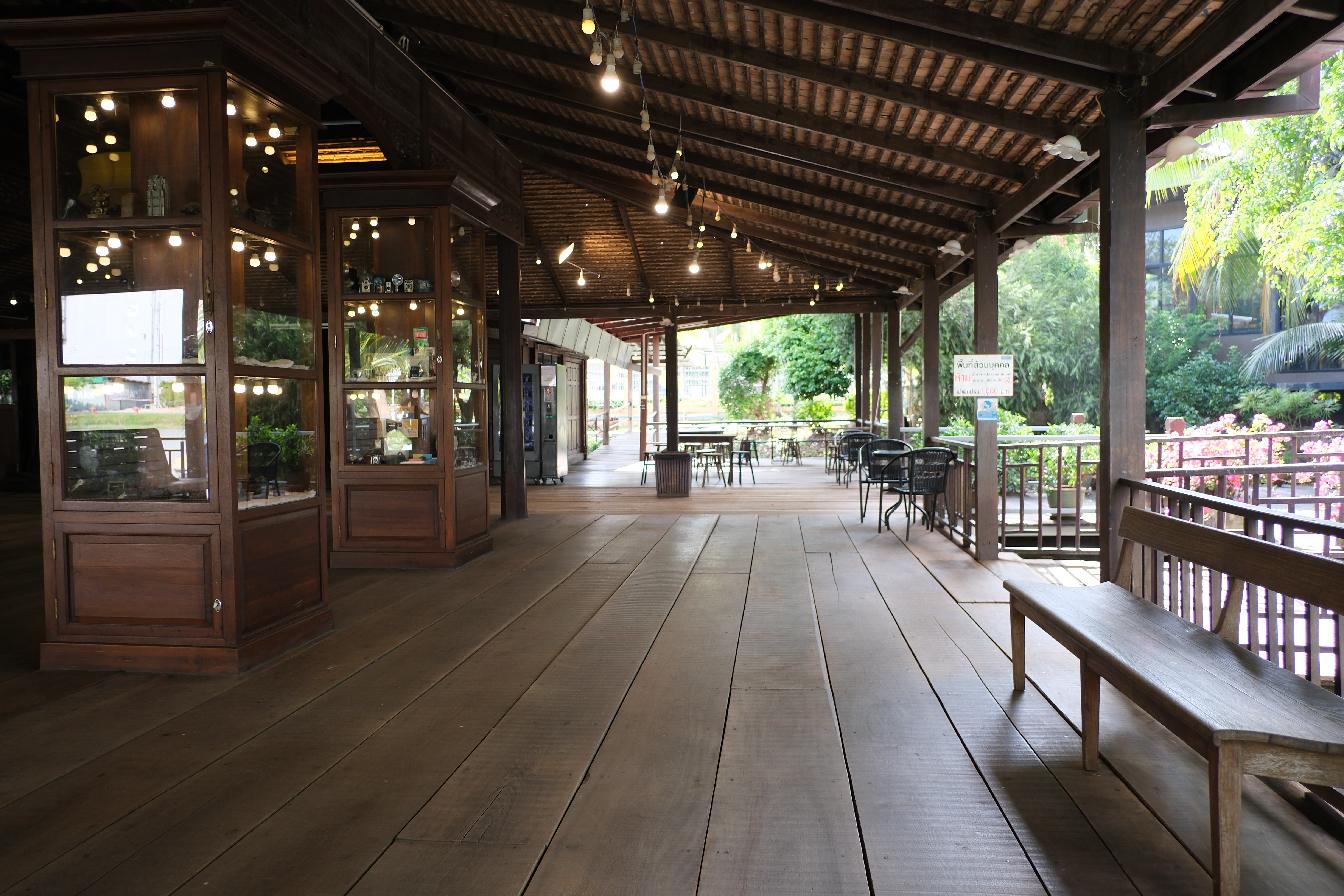 Covered wooden veranda with a waiting bench, hanging lights and outdoor tables beyond