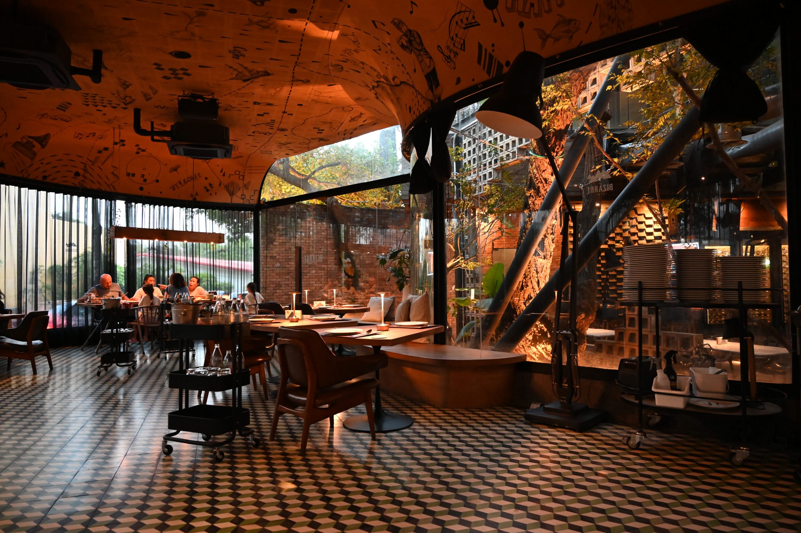 Restaurant dining room with patterned tile floor, wooden tables of different sizes and tall windows onto a courtyard